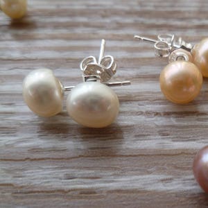 Picture shows 3 pairs of circular pearl stud earrings, with silver post and scroll back/butterfly fixings. Colours shown are white, peach and pink.