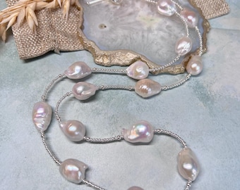 Könnte beinhalten: Eine lange silberne Kettenkette mit weißen Barockperlen. Die Kette ist mit zwei Strängen Perlen und silbernen Perlen geschichtet.