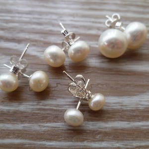 Picture shows 4 pairs of circular, white coloured pearl stud earrings, with silver post and scroll back/butterfly fixings. Earrings are of varying sizes.