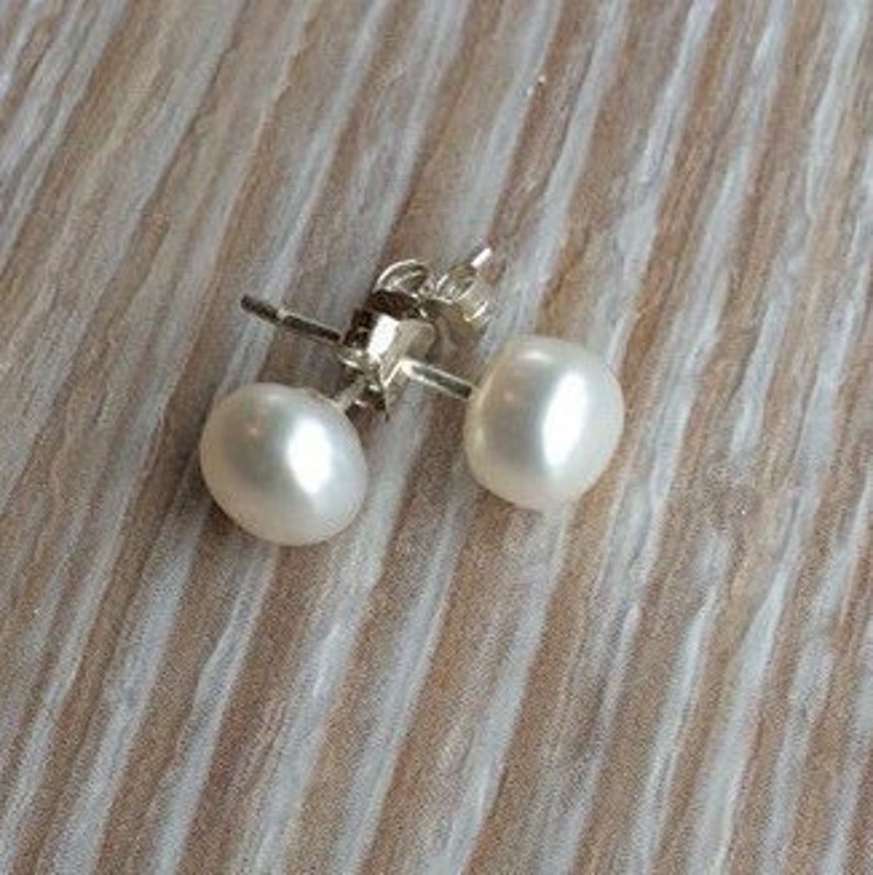 Picture shows a pair of circular, white coloured pearl stud earrings, with silver post and scroll back/butterfly fixing.