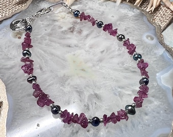 Könnte beinhalten: Ein silbernes Kettenarmband mit rosa und schwarzen Perlen. Das Armband hat einen kleinen Anhänger mit einem Design darauf.