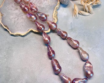 Könnte beinhalten: Eine lange Halskette aus schillernden rosa Barockperlen. Die Perlen sind auf einer silbernen Kette aufgefädelt und haben unterschiedliche Größen. Die Halskette wird auf einer hellblauen Oberfläche präsentiert.