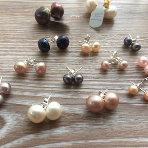 Picture shows several pairs of circular, pearl stud earrings, with silver post and scroll back/butterfly fixings. Earrings shown are of various sizes and colours.