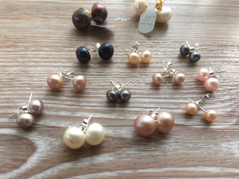 Picture shows several pairs of circular, pearl stud earrings, with silver post and scroll back/butterfly fixings. Earrings shown are of various sizes and colours.