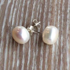 Picture shows a pair of circular, white coloured pearl stud earrings, with silver post and scroll back/butterfly fixing.