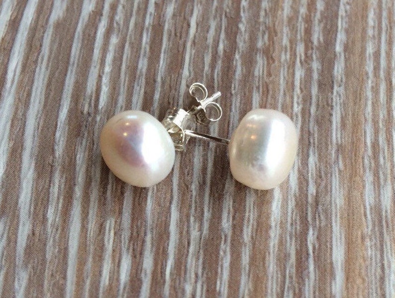 Picture shows a pair of circular, white coloured pearl stud earrings, with silver post and scroll back/butterfly fixing.