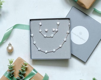 Könnte beinhalten: Ein silbernes Halsketten- und Ohrring-Set mit perlmuttartigen Sternanhängern in einer grauen Box mit dem Text "Pearls & Daughters".
