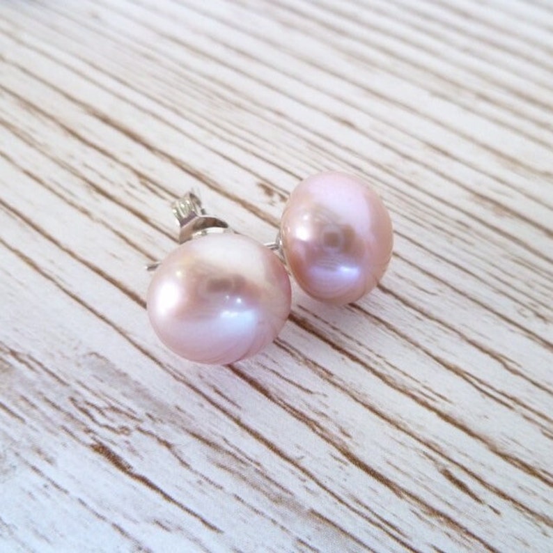 Picture shows a pair of circular, pink coloured pearl stud earrings, with silver post and scroll back/butterfly fixings.