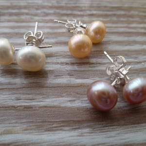 Picture shows 3 pairs of circular pearl stud earrings, with silver post and scroll back/butterfly fixings. Colours shown are white, peach and pink.