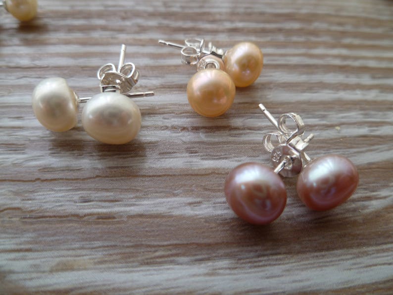 Picture shows 3 pairs of circular pearl stud earrings, with silver post and scroll back/butterfly fixings. Colours shown are white, peach and pink.