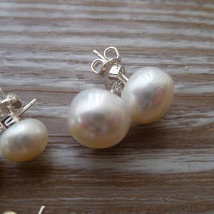 Picture shows a pair of circular, white coloured pearl stud earrings, with silver post and scroll back/butterfly fixing. A smaller pair of the same type of earring also feature in the picture.