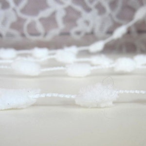 May include: White pom-pom trim with a white string connecting the pom-poms.