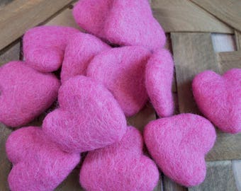 May include: A group of pink felt hearts, arranged in a pile on a wooden surface. The hearts are soft and fuzzy, and they are perfect for Valentine's Day or any other occasion.