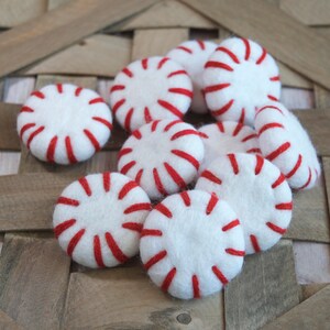 May include: A group of felt peppermint candies in white with red stripes. The candies are arranged in a basket.