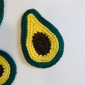 May include: Two crocheted avocado shapes, one green and yellow with a brown pit, the other partially visible in the background.