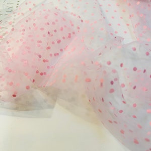 May include: Pink tulle fabric with small pink polka dots. The fabric is sheer and delicate.