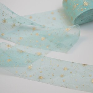 May include: A roll of light blue tulle ribbon with gold glitter stars. The ribbon is rolled up and the ends are loose.
