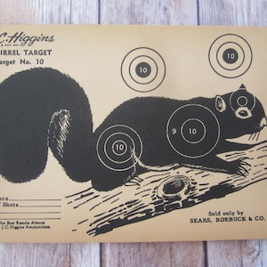 May include: A vintage paper squirrel target for shooting practice. The target features a black silhouette of a squirrel on a brown branch with a 10, 9, and 10 point scoring system. The text "J.C. Higgins Squirrel Target Target No. 10" is printed at the top of the target. The text "Sold only by SEARS, ROEBUCK & CO." is printed at the bottom of the target.