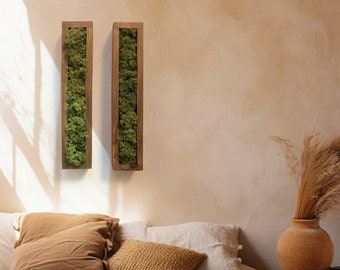 Puede incluir: Dos marcos de madera rectangulares con musgo verde preservado en su interior, colgados en una pared beige sobre una cama con ropa de cama marrón y blanca. Un jarrón con hierba seca se encuentra en una cesta tejida junto a la cama.