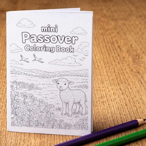 May include: A mini Passover coloring book with a lamb illustration, clouds, and the text "mini Passover Coloring Book." Two colored pencils, purple and green, are in the foreground. The book is on a wooden surface.