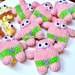 May include: Handmade crochet Patrick Star plush toys. The pink starfish-shaped toys have green shorts with purple accents, black and white eyes, and smiling faces. The text "Art Bloom Crochet" is visible.