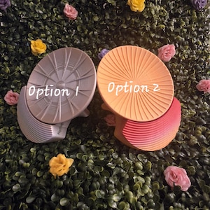 May include: Two decorative, abstract sculptures. Option 1 is a silver-gray color with a radial design. Option 2 is orange with a radial design and a red-orange gradient base. The text "Option 1" and "Option 2" are written on the sculptures.