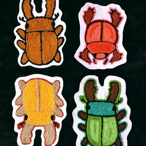 May include: Four embroidered insect patches in various colors: brown, red-orange, yellow-orange, and green. Each patch has a white border and is stitched with detailed textures, showcasing the insects' forms against a black background.