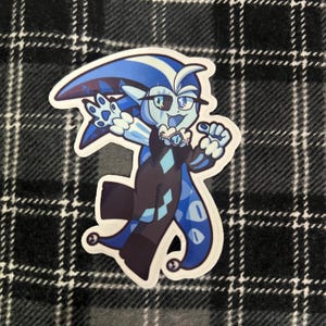 May include: A sticker featuring a cartoon character with blue skin, a dark blue outfit, and a white collar. The character has a large head with a pointed hat and is making a playful gesture. The sticker is on a black and white plaid background.