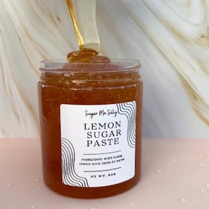 May include: A jar of lemon sugar paste with a white label featuring the text "Lemon Sugar Paste" and the brand name "Sugar Me Silly." The ingredients are listed below the text. A stream of the paste is pouring into the jar. The net weight is 8 oz.