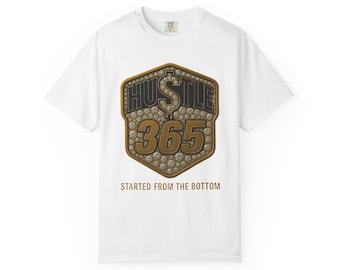 May include: White t-shirt with a gold and black graphic. The graphic features the word "HUSTLE" above the number "365" and the phrase "STARTED FROM THE BOTTOM". The design includes diamond-like embellishments.