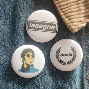 May include: Three white circular badges with various designs. One badge displays the word "lasagne" in a black box. Another features a cartoon image of a man wearing sunglasses. The third badge has the word "oasis" within a laurel wreath.