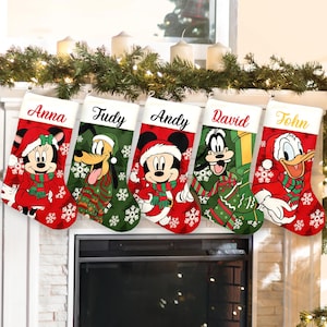 May include: Five personalized Christmas stockings featuring Disney characters Minnie Mouse, Pluto, Mickey Mouse, Goofy, and Donald Duck. Each stocking has a white cuff with a name printed in script: Anna, Fudy, Andy, David, and John.