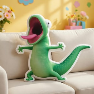 May include: A green lizard-shaped plush pillow with a wide open mouth and pink tongue. The pillow has a white outline and is sitting on a beige couch. The lizard has outstretched arms and a long tail.