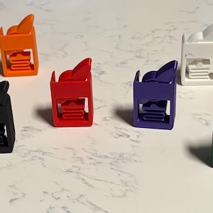 Può includere: Una collezione di sei piccole clip rettangolari in plastica in vari colori solidi, tra cui arancione, nero, rosso, viola, bianco e verde. Ogni clip presenta un meccanismo a leva sulla parte superiore e una presa interna scanalata.
