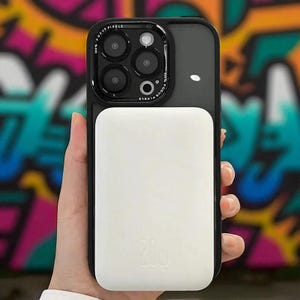 Puede incluir: Una funda de teléfono negra y blanca con una base de carga blanca. La funda tiene un módulo de cámara con el texto "100% FOCUS PIXELS". La base de carga tiene el texto "20w".