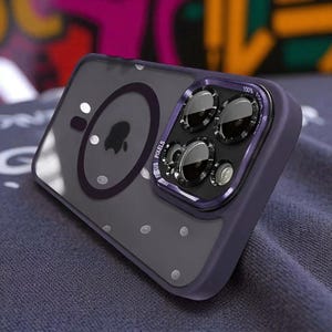 Puede incluir: Una funda transparente para teléfono con un protector de lente de cámara púrpura. La funda tiene una parte trasera transparente con detalles de puntos blancos y un borde púrpura. El protector de la cámara tiene el texto "FOCUS PIXELS" y "100% FOCUS".