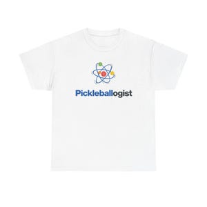 May include: White t-shirt with the word "Pickleballogist" in blue, below a graphic of an atom with green, red, and yellow spheres. The shirt is made of a soft material and has a crew neck.