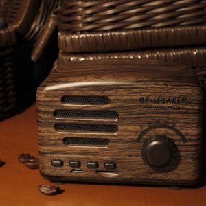 Peut inclure: Un petit haut-parleur BT de style r&eacute;tro avec une finition imitation bois. Le haut-parleur a un cadran, des boutons et le texte "BT SPEAKER MULTIMEDIA COMBINING". Des grains de caf&eacute; sont &eacute;parpill&eacute;s devant le haut-parleur.