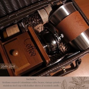 Peut inclure: Un panier en osier marron rempli d'articles li&eacute;s au caf&eacute;. Il comprend un moulin &agrave; caf&eacute; en bois, une tasse en acier inoxydable avec un manchon en cuir, un pot de grains de caf&eacute; et une bougie parfum&eacute;e. Le texte "Rustic Roast" est visible.