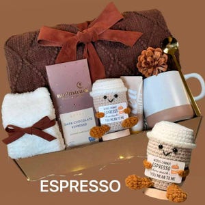 以下が含まれることがあります： 茶色をテーマにしたギフトボックス。茶色の毛布、ダークチョコレート、白と茶色のマグカップ、ローション、白いタオル、そして「WORDS CANNOT ESPRESSO how much YOU MEAN TO ME」というテキストが入った2つのかぎ針編みのコーヒーカップが含まれています。