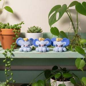 May include: Three small, light blue clay mouse figurines, each featuring large rounded ears, a pink nose, and a small piece of yellow Swiss cheese resting on top of their heads. The mice have painted black eyes and rounded paws.