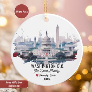 May include: A white ceramic ornament featuring a watercolor illustration of Washington D.C. landmarks, including the Capitol Building and Washington Monument. Text reads "WASHINGTON D.C. The Smith Family Family Trip 2025". Includes a gold hanging cord.