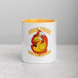 May include: White ceramic mug with a yellow interior. The mug features a cartoon duck wearing a top hat and bow tie, set against a red flame design. The text "TAKE THAT DEPRESSION" is printed on the mug.