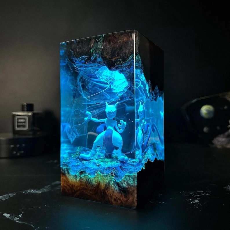 Peut inclure: Sculpture rectangulaire en r&eacute;sine repr&eacute;sentant Mewtwo bleu. L'int&eacute;rieur de la sculpture est bleu et lumineux, avec une base en bois et des accents sombres. L'&oelig;uvre est illumin&eacute;e, cr&eacute;ant un effet visuel saisissant.