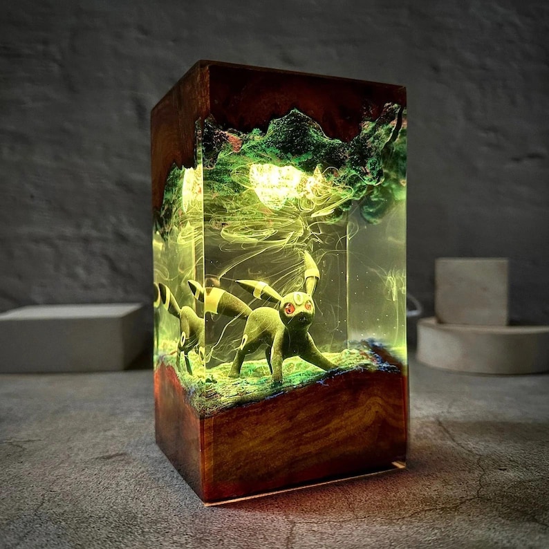 Peut inclure: Lampe rectangulaire en bois avec un int&eacute;rieur lumineux mettant en vedette une figurine de cr&eacute;ature verte. L'int&eacute;rieur de la lampe a une palette de couleurs verte et jaune, avec un dessus rouge fonc&eacute; et une base en bois. La figurine a des yeux rouges et des accents noirs.