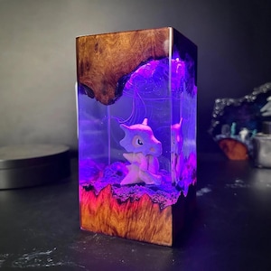 Peut inclure: Pi&egrave;ce d'art en r&eacute;sine rectangulaire avec un personnage de Cubone &agrave; l'int&eacute;rieur. Le haut et le bas sont en bois, le centre brille en violet. Le bois a un grain naturel, et la r&eacute;sine a un effet orange et violet. Objet d&eacute;coratif unique.