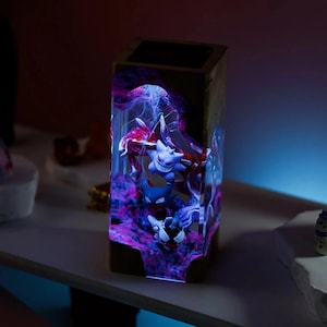 Peut inclure: Lampe rectangulaire en r&eacute;sine avec un design Gengar et Haunter. L'ext&eacute;rieur est en bois fonc&eacute; et l'int&eacute;rieur est vibrant avec des motifs tourbillonnants violets et bleus. Les figurines sont visibles dans la r&eacute;sine.