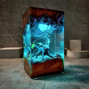 Peut inclure: Lampe rectangulaire en r&eacute;sine avec une figurine Umbreon sombre dans un environnement bleu et violet lumineux. La lampe est encadr&eacute;e de bois brun fonc&eacute;. L'ensemble cr&eacute;e une ambiance mystique et enchanteresse.