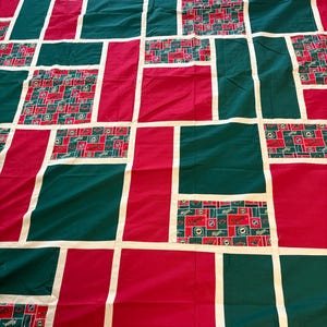 Puede incluir: Un edredón de patchwork con un diseño geométrico. Presenta cuadrados rojos, verdes y estampados, separados por tiras blancas. Los cuadrados estampados tienen un diseño rojo, verde y blanco.