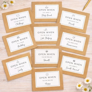 May include: A collection of brown paper cards with white borders and black text. Each card reads "Open When" followed by a specific sentiment, such as "You're facing a challenge" or "You're feeling lonely."